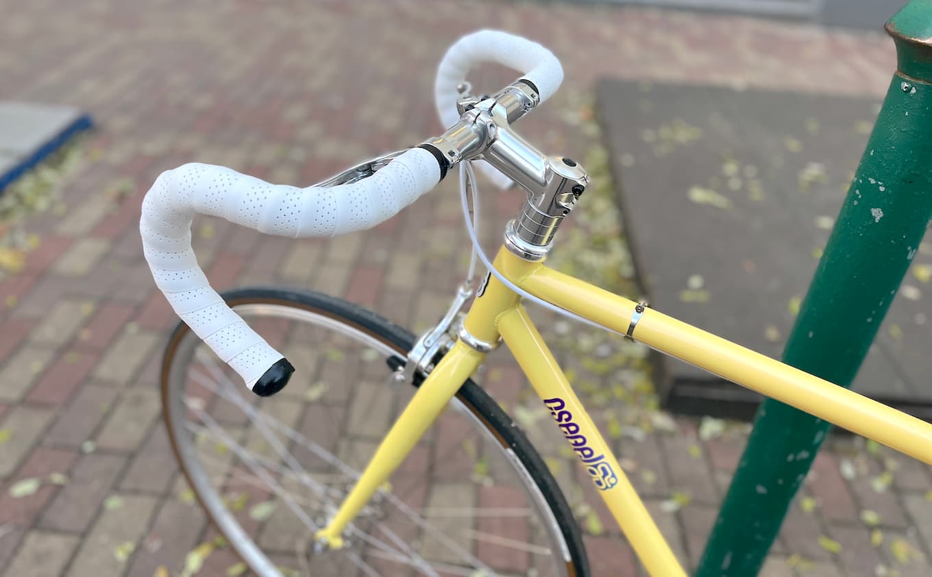A yellow road bike-type single speed bicycle with drop bars and white bar tape