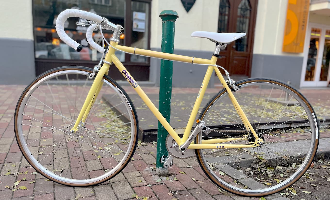 A light yellow single speed, road-bike type bicycle with white drop bars and white saddle.